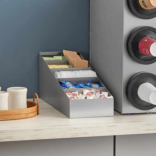 A ServSense stainless steel lid and condiment packet organizer on a counter.