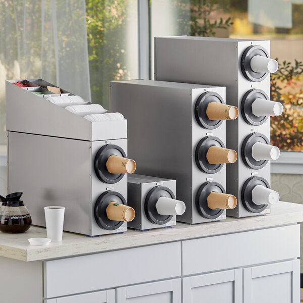 A KleanTake stainless steel countertop cup dispenser with lid and straw organizers holding cups.