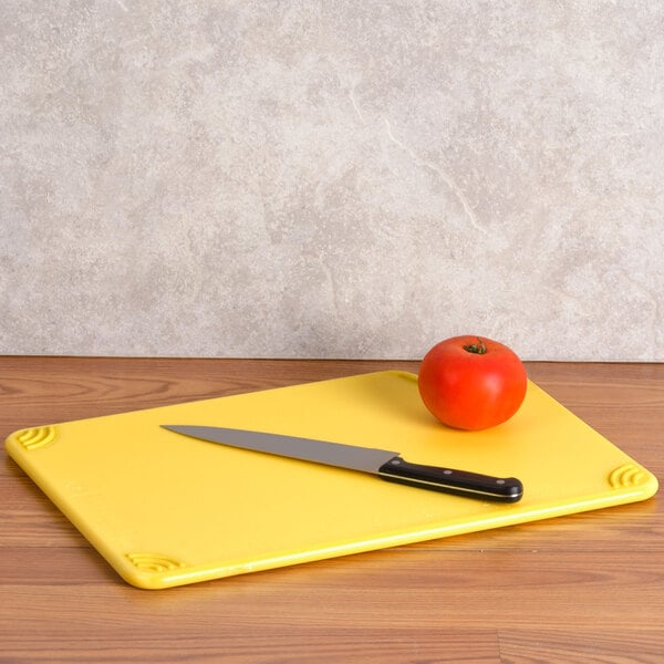 A San Jamar yellow cutting board with a knife cutting a tomato.