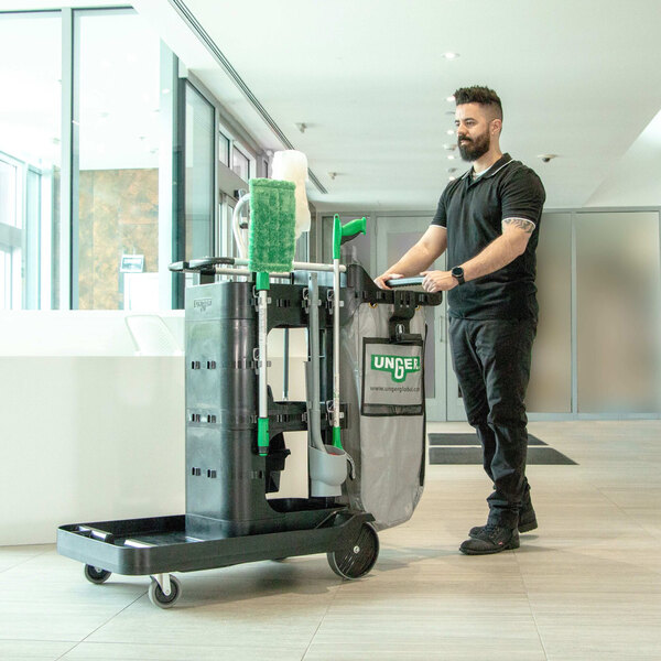 A man pushing a Unger ZoneCleanRx janitorial cart with a green machine.