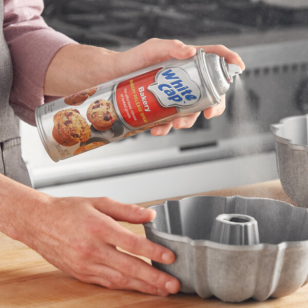 A person holding a can of White Cap Bakery release spray spraying a cake pan.