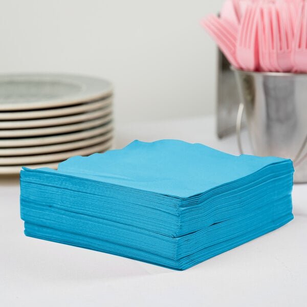 A stack of turquoise blue Creative Converting paper napkins on a table.