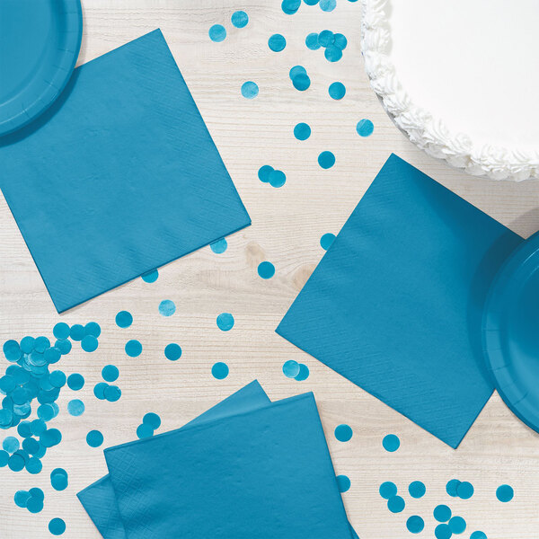 A table with turquoise blue napkins and confetti.