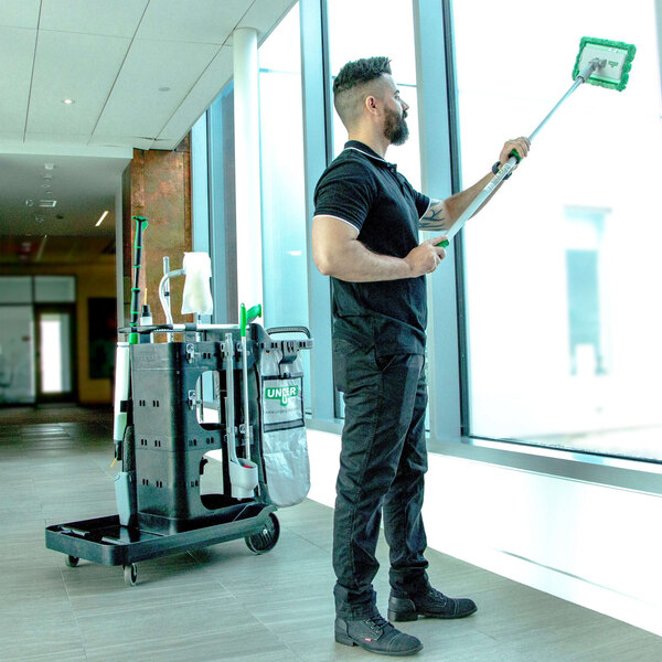 A man using an Unger SpotCleanRx Janitorial Cart to clean a window with a mop.