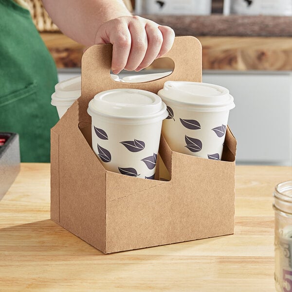 A person holding a brown box with white coffee cups inside.