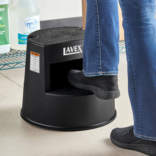 A person's foot stepping on a black Lavex rolling step stool.