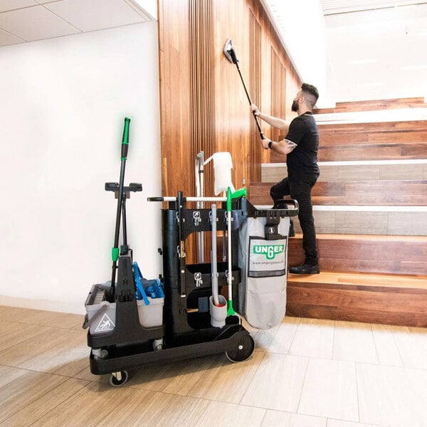 A man in a black shirt using an Unger Deep Cleaning Janitorial Cart to clean a staircase with a mop and broom.