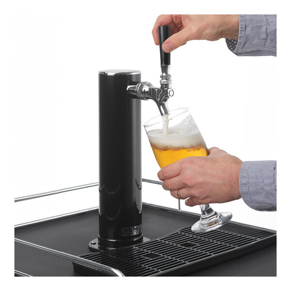 A person pouring a beer from a Danby kegerator tap into a glass.