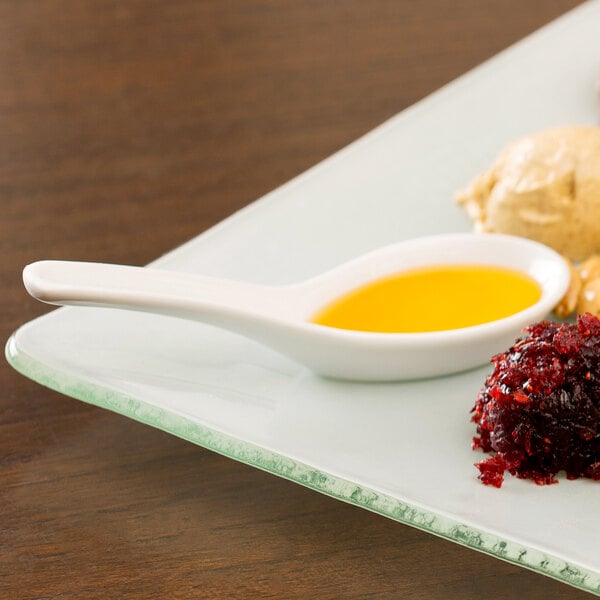 A plate of food with a 10 Strawberry Street white porcelain Chinese wonton spoon and sauce.