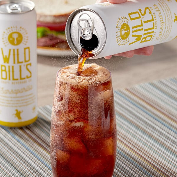 A hand pours Wild Bill's Sarsaparilla soda from a can into a glass.