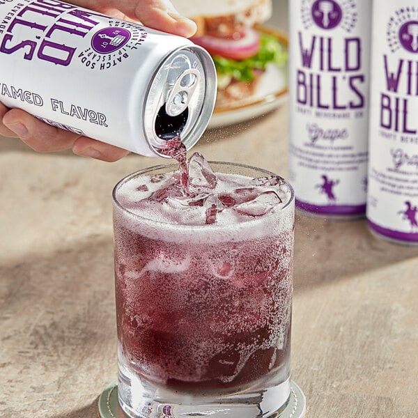 A hand pouring Wild Bill's Grape Soda into a glass filled with ice.