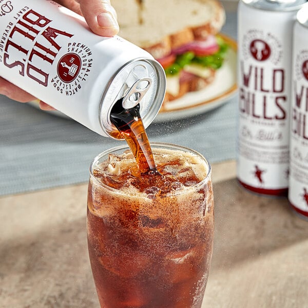 A hand pouring Wild Bill's Dr. Bill's soda from a can into a glass of ice.