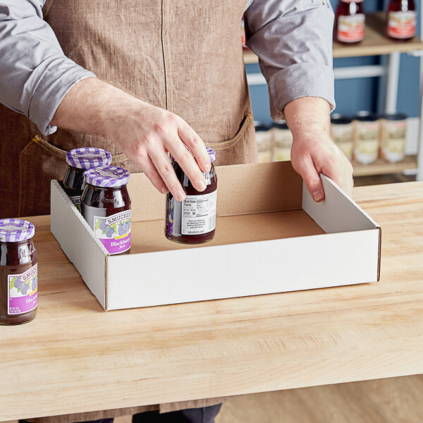 A person holding two jars of jam in a white corrugated half tray.