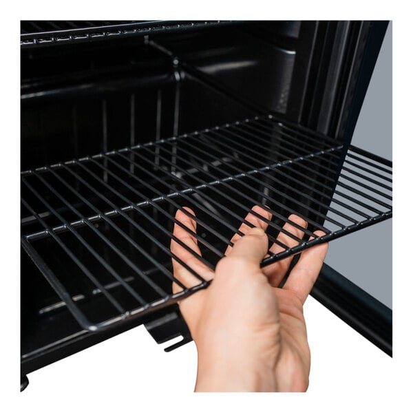 A hand adjusting a wire shelf inside a stainless steel glass door beverage refrigerator.