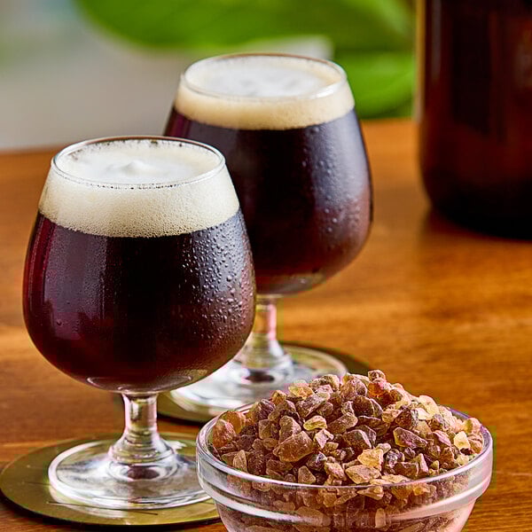 A bowl of Roses Dryden and Palmer brown rock candy on a table with a glass of dark liquid.
