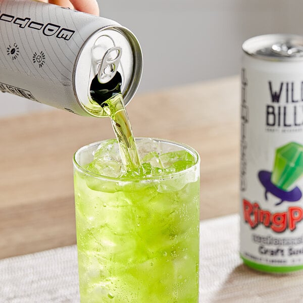 A can of Wild Bill's Ring Pop Watermelon Soda pouring green liquid into a glass on a table.