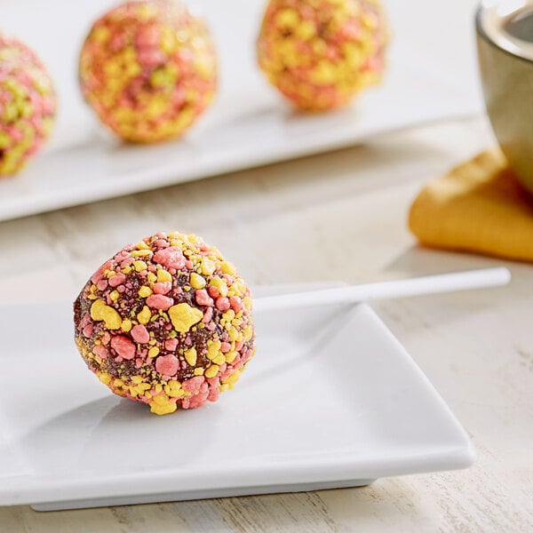 A round doughnut with pink and yellow Yum Crumbs on a table.