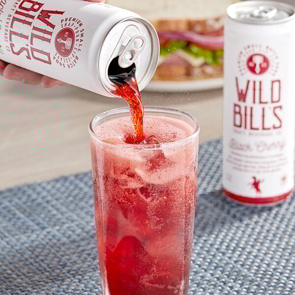 A hand pouring Wild Bill's Black Cherry Soda into a glass of ice.