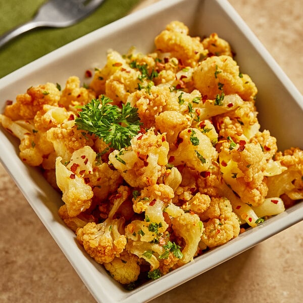 A white bowl of fresh cauliflower florets with parsley and spices.