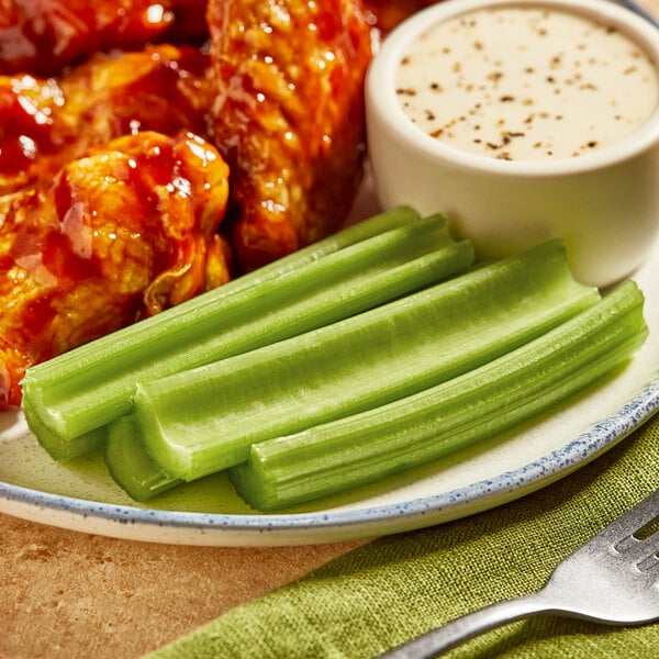 A plate of chicken wings with celery sticks and dipping sauce on a table.