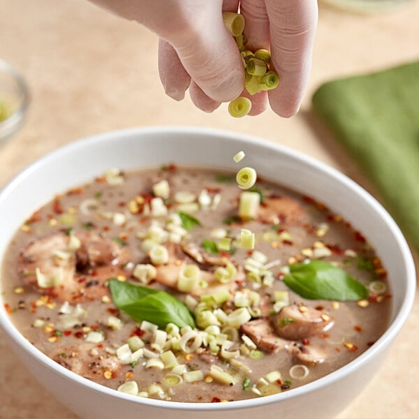 A person sprinkling fresh lemongrass into a bowl of soup.