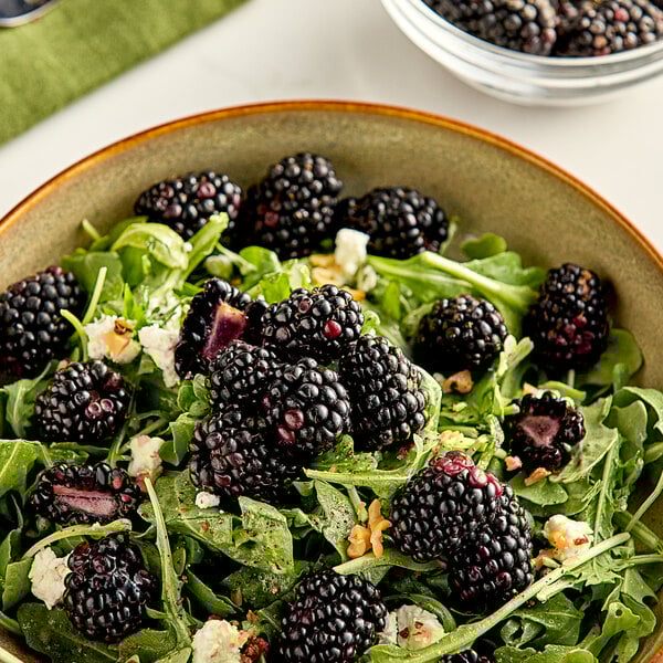 A bowl of mixed greens with blackberries.