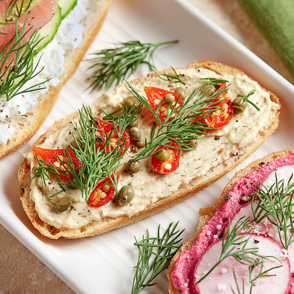 A sandwich with a spread, cucumber, and fresh dill on a table.