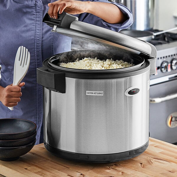 A woman using a Galaxy 90 Cup Electric Rice Warmer to cook rice in a professional kitchen.