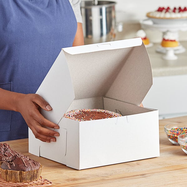 A person holding a white Baker's Lane cake box.