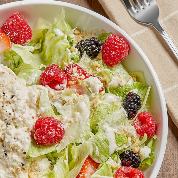 A bowl of salad with fruit and a fork on a white background.