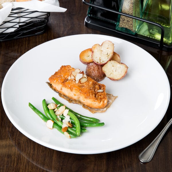 A Libbey Porcelana bright white round porcelain coupe plate with a piece of salmon and green beans on a table.