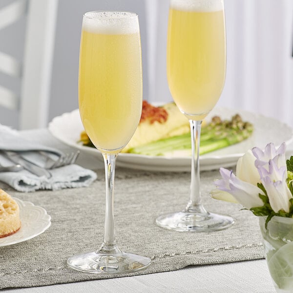 Two Libbey Vina flute glasses filled with yellow liquid on a table.