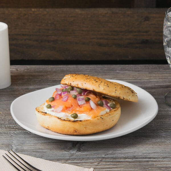 A Libbey Porcelana bright white porcelain coupe plate with a bagel with salmon and onions on it.