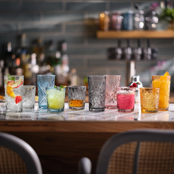A collection of colorful Libbey Hobstar 12 oz. rocks and double old fashioned glasses displayed on a bar counter.