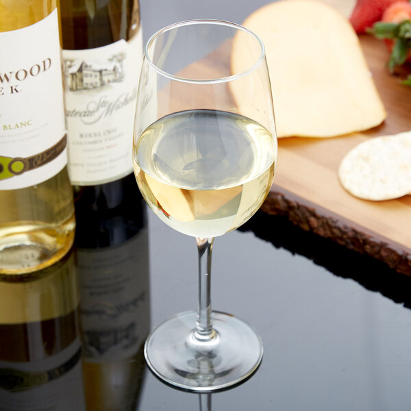 A Libbey white wine glass filled with white wine on a table next to a bottle of white wine.