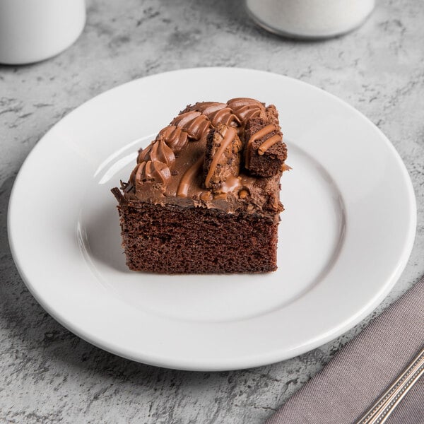 A piece of chocolate cake with frosting on a Libbey Porcelana white plate.