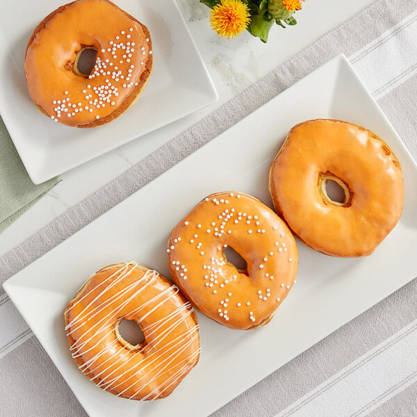 A plate of three donuts with orange glaze and white sprinkles.