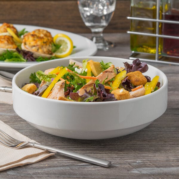 A Libbey Porcelana bright white porcelain bowl filled with salad and a fork on a table.