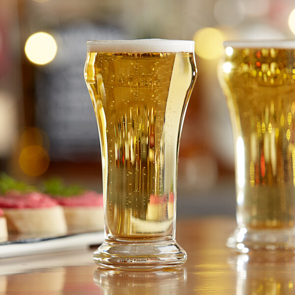 A pair of Libbey Pilsner glasses filled with beer on a table.