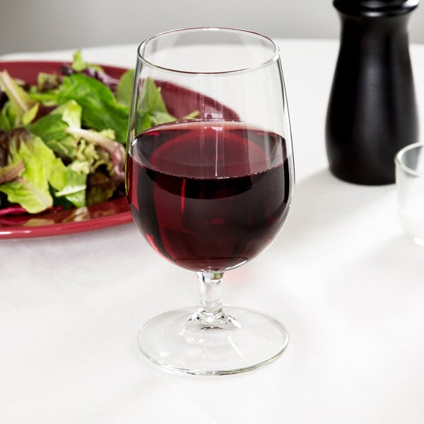 A Libbey Vina goblet of red wine next to a plate of salad.