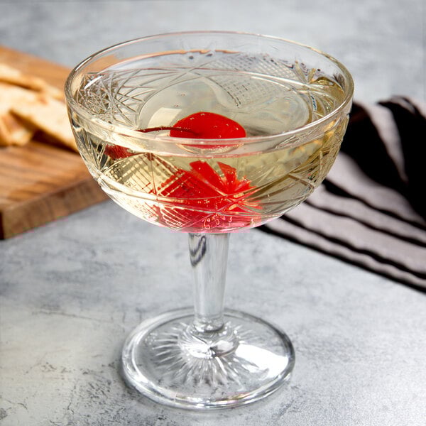 A Libbey Hobstar coupe cocktail glass with liquid and a cherry in it.
