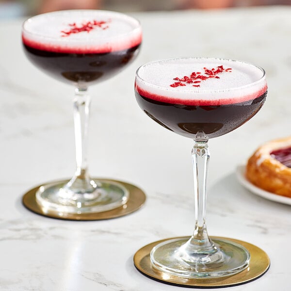 Two glasses of red liquid on a table with a donut.