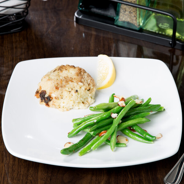 A Libbey Porcelana square porcelain coupe plate with food including green beans and a lemon on a table.