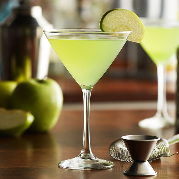 A Libbey martini glass filled with green liquid with a slice of green apple on the rim.