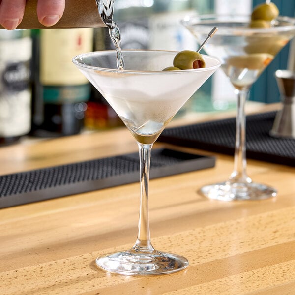 A clear Libbey Vina 8 oz. martini glass with a stem, shown with olives and being filled with liquid.