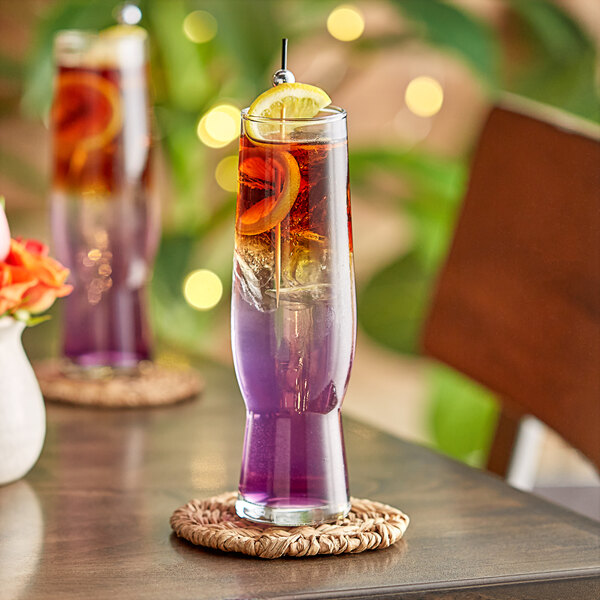 A Libbey flute glass of purple liquid with a lemon wedge on a coaster.