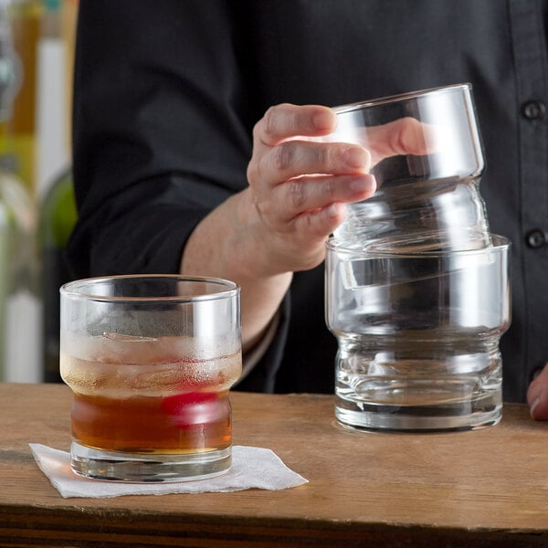 A person pouring a brown liquid into two Libbey Newton Stackable Rocks glasses on a table.