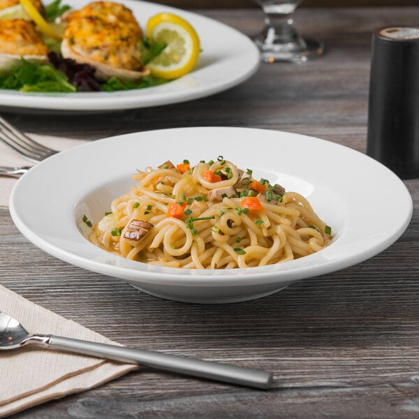 A bowl of noodles with vegetables and meat in a Libbey Porcelana soup bowl on a table.