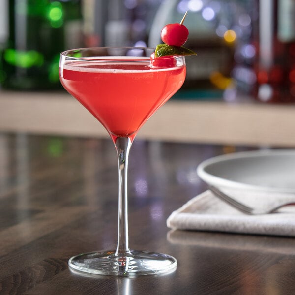 A glass of pink liquid with a cherry on top sits on a table.
