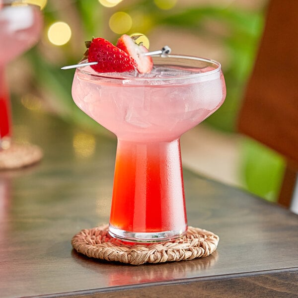 A Libbey coupe glass filled with a pink drink and a strawberry on the rim.